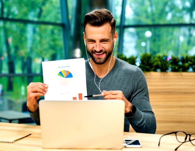 Confident smiling young businessman showing diagrams online using his laptop at office desk